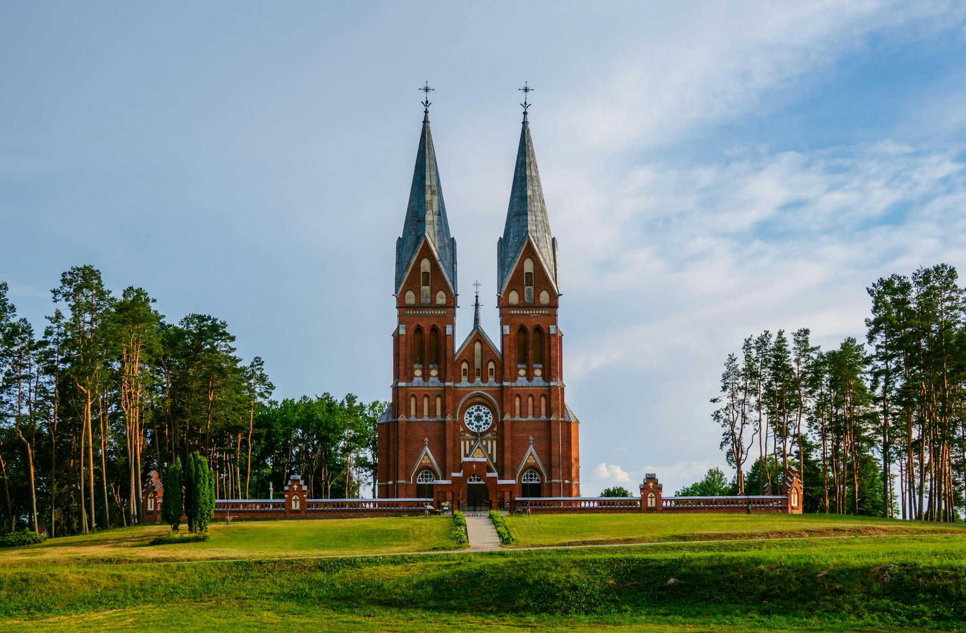 Ceglany kościół rzymskokatolicki na tle zielonego krajobrazu