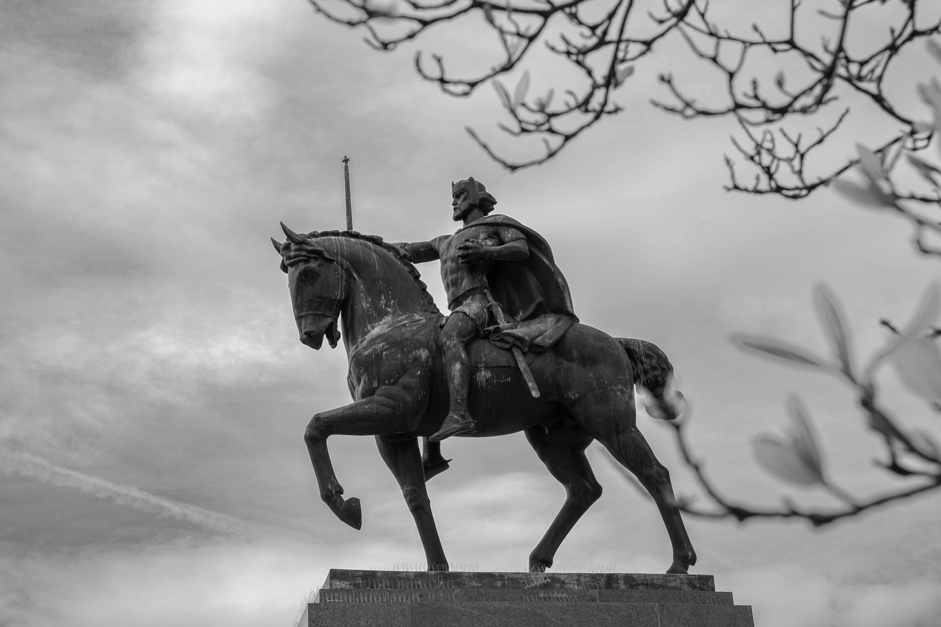 Czarno-białe zdjęcie pomnika króla na koniu na tle miasta