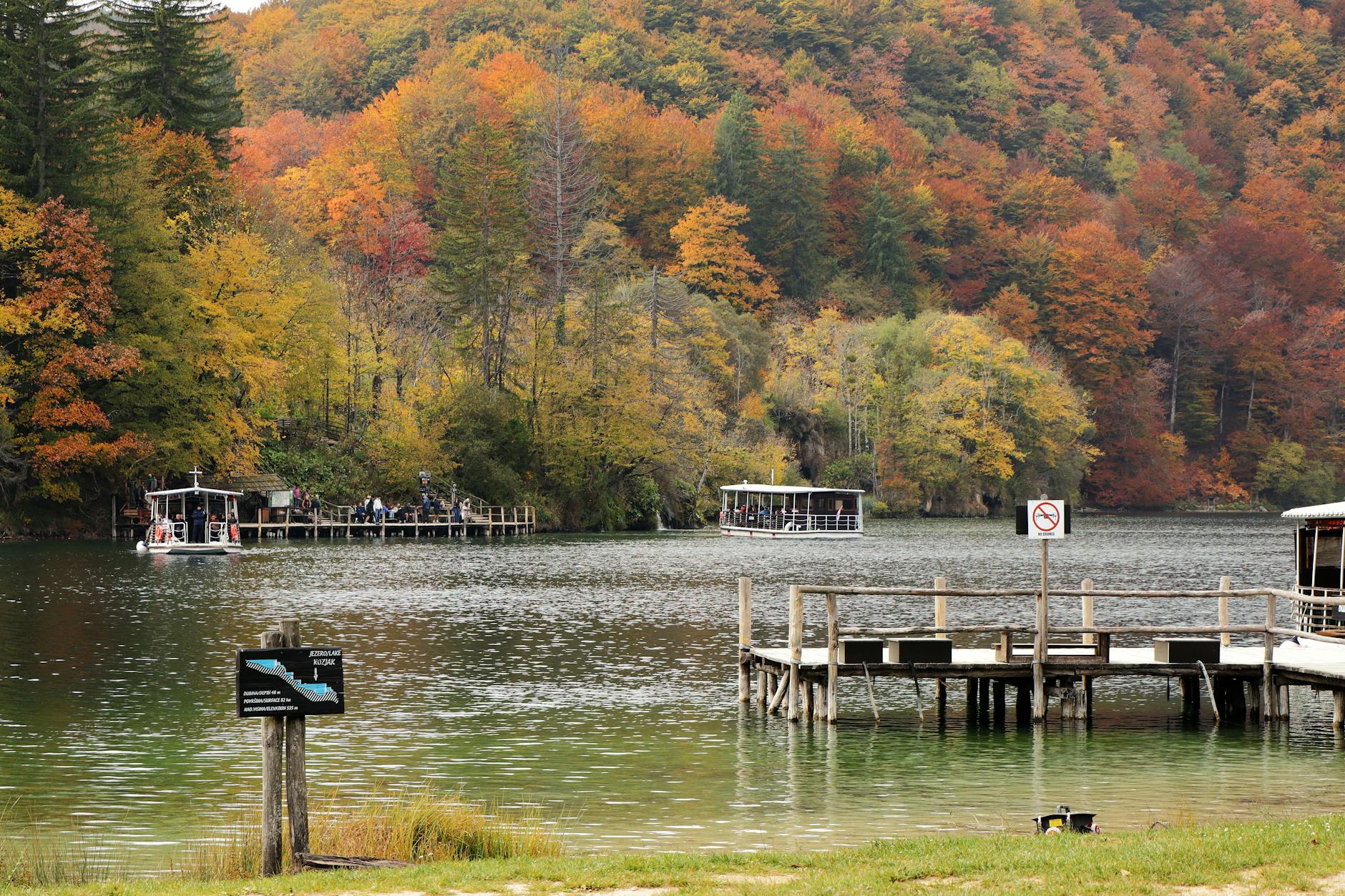 Drewniany pomost z łódkami na spokojnym jeziorze w jesiennych barwach