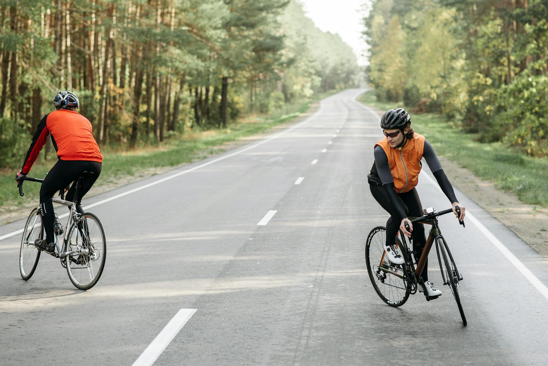 Dwóch rowerzystów jedzie pustą szosą przez zielony las