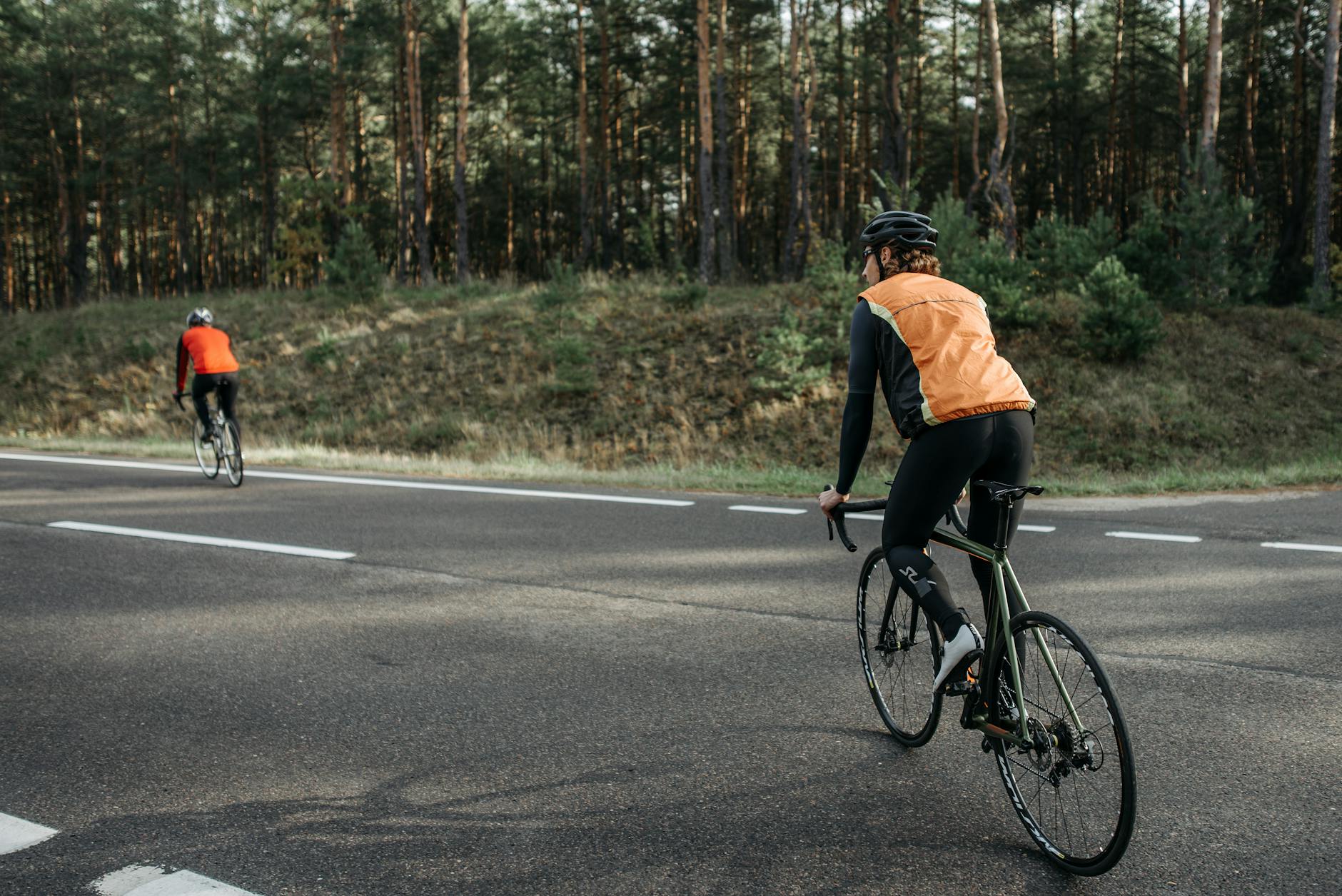 Dwójka rowerzystów w kamizelkach odblaskowych jedzie leśną drogą