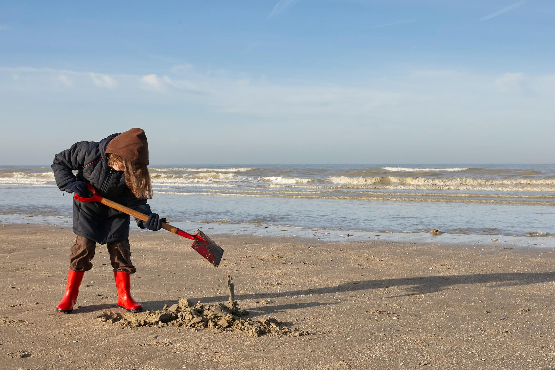 Dziecko w czerwonych kaloszach bawi się w piasku na słonecznej plaży
