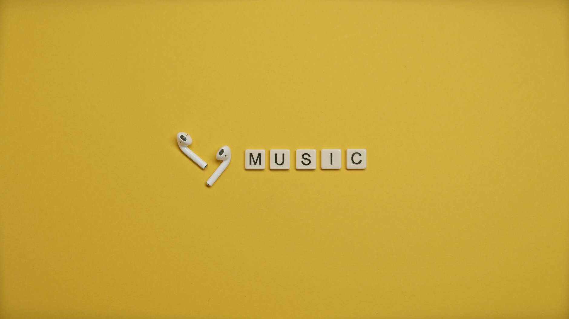 Białe słuchawki bezprzewodowe i literki muzyczne na żółtym tle
