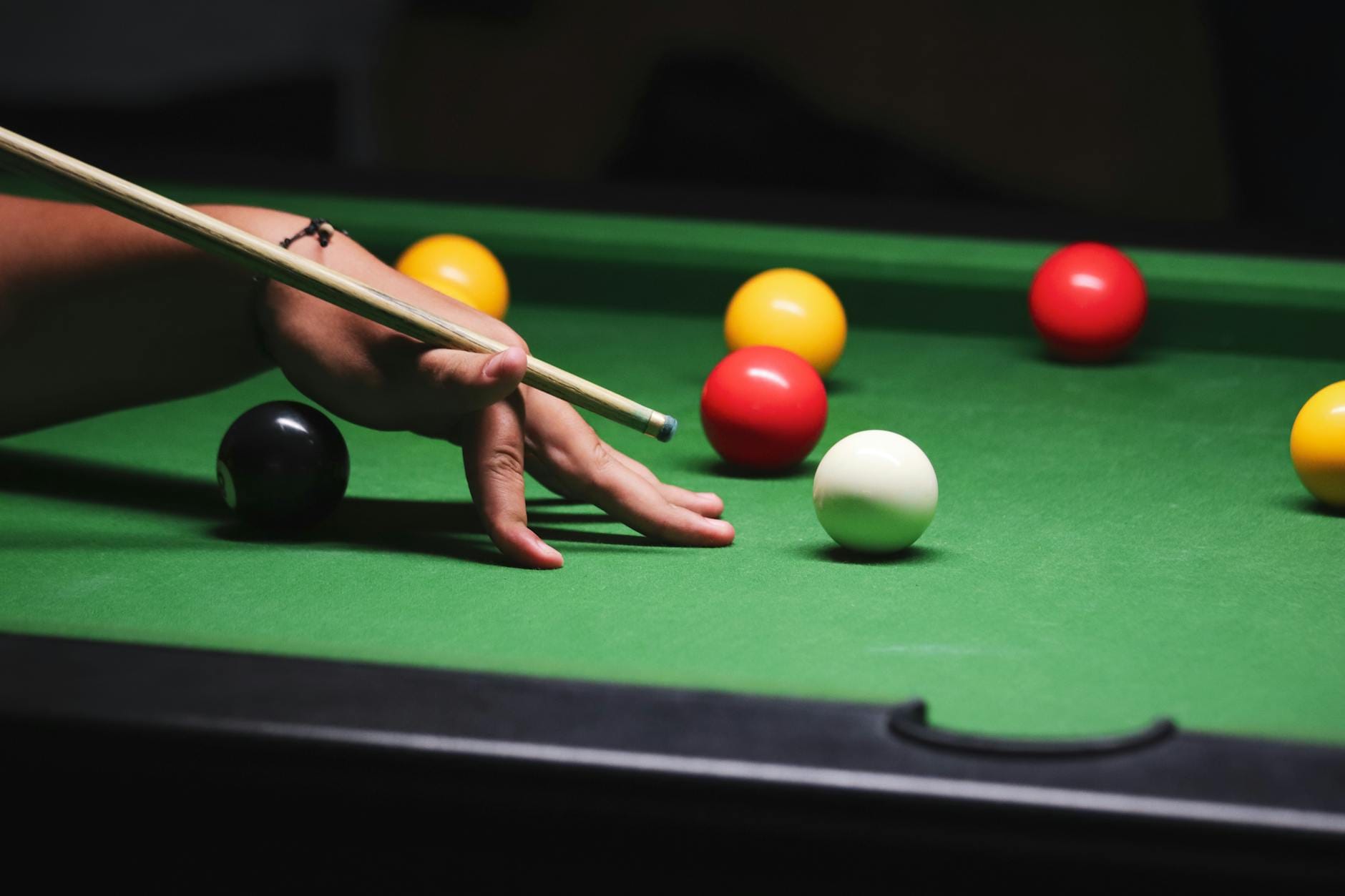 Ręka ustawiająca kij bilardowy przy białej bili na stole z kolorowymi kulami