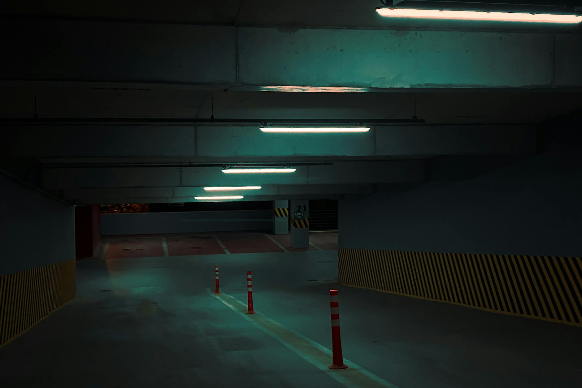 Słabo oświetlony podziemny parking z białymi świetlówkami i pachołkami