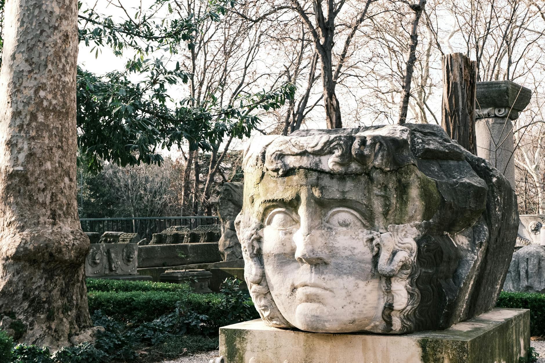 Kamienna rzeźba twarzy wśród drzew w skansenie archeologicznym