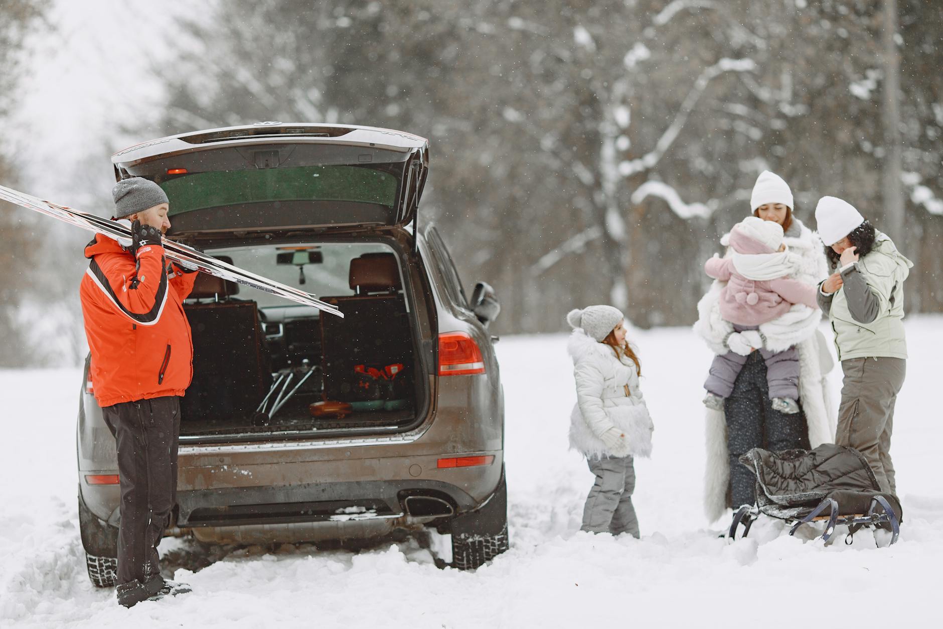 Rodzina wyciąga narty i sanki z samochodu na ośnieżonym parkingu