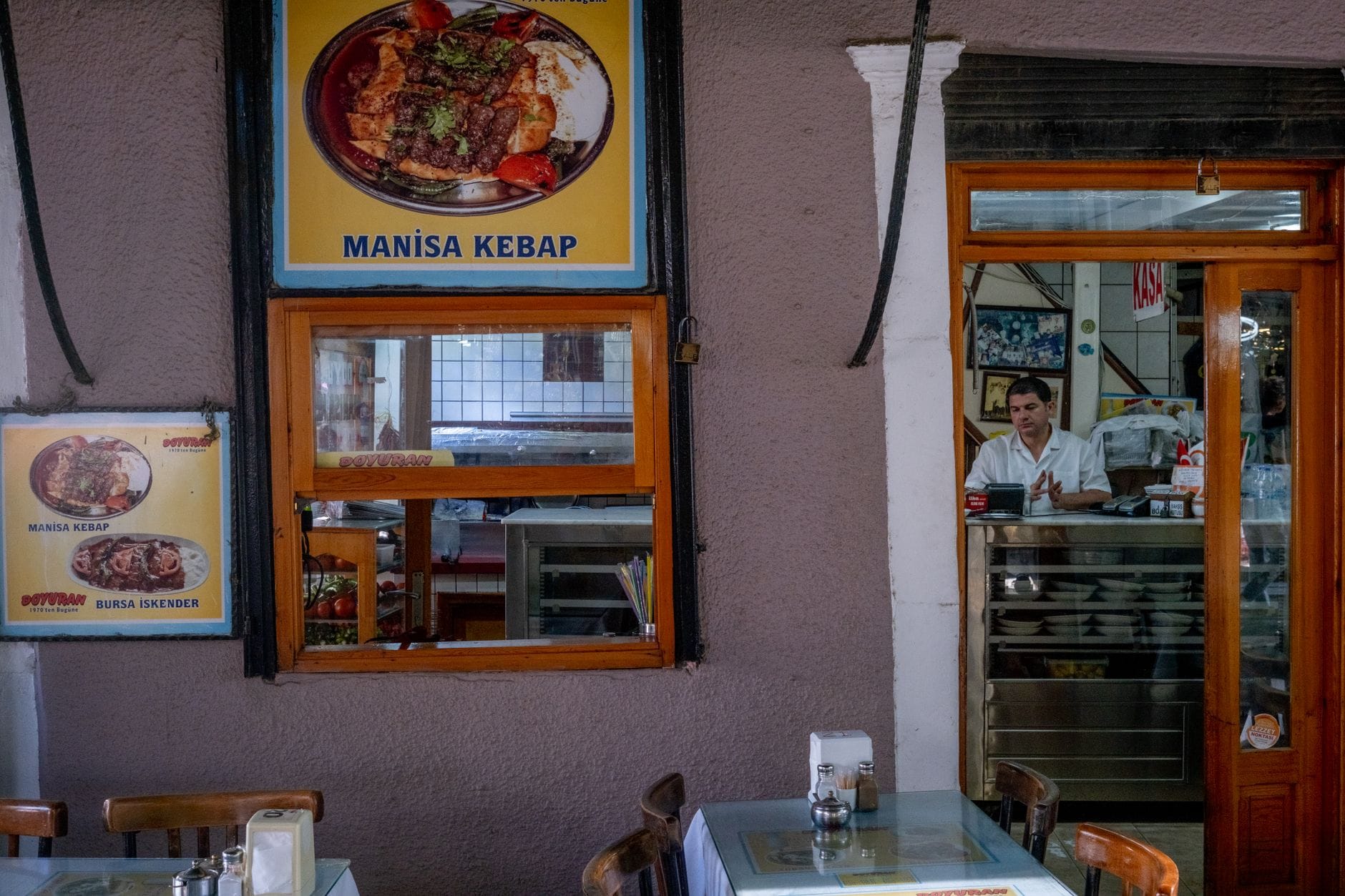Kelner przy ladzie w przytulnej tureckiej restauracji z plakatami kebabów